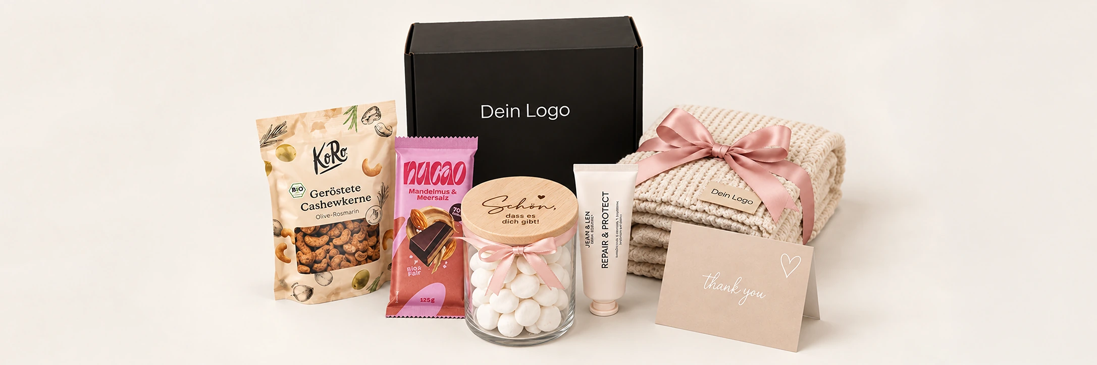 Geschenkidee mit schwarzer Logobox, Cashewkernen, Schokolade, personalisiertem Süßigkeitenglas, Creme, cremefarbenem Handtuch mit Logo und Dankeskarte